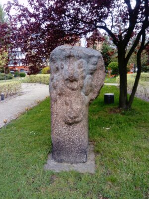 Zdjęcie przedstawia rzeźbę od frontu, wykonaną z jednego bloku granitowego, schematycznie obrobioną, o kształcie amorficznym, abstrakcyjnym, z przypominającymi roślinność i stworzenia morskie motywami.