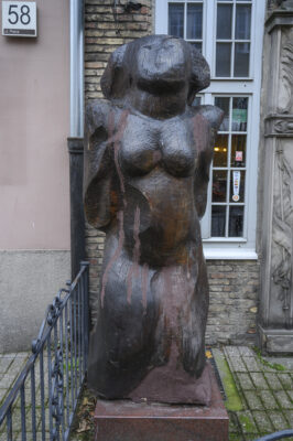 A sculpture made of dark wood, synthetically obtained, a massive figure of a woman posed in a counterpoint; the woman's body is made of solid blocks without any anatomical details (including no hands or feet); a face with only the suggested lines of the eyes, nose, smile
