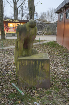 Zdjęcie pionowe wykonane na wprost przedstawiające kamienną rzeźbę, która jest ustawiona na sześciennym postumencie. Figura i postument zostały wykonane z tego samego, ciemnoszarego kamienia a ich powierzchnia zaczyna być porośnięta różnymi porostami. Antropomorficzna figura ma charakter abstrakcyjny i przypomina postać kobiety, która to opiera się na dłoniach o sześcian, głowę zaś ma zarzuconą do tyłu. Granice pomiędzy dwoma bryłami są bardzo zatarte.