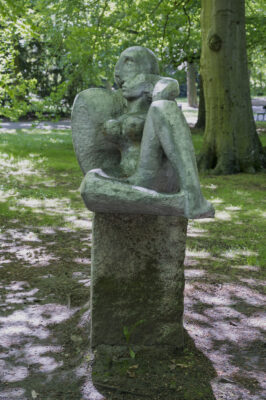 Zdjęcie pionowe wykonane na wprost przedstawiające kamienną rzeźbę, na której konstrukcje składają się dwie, siedzące figury ludzkie. Sprawiają one wrażenie jakby opierały się wzajemnie o swoje plecy. Figury mają obły kształt oraz wydłużone proporcje, a elementy anatomiczne budowy ciała takie jak: oczy, nos, usta, czy kobiece piersi są zaznaczone w sposób delikatny, jak również nie wzbudzają wątpliwości co do ich zgodności biologicznej. Rzeźba została wykonana z jasnoszarego kamienia i jest umieszczona na sześciennym postumencie wykonanym w tym samym materiale.