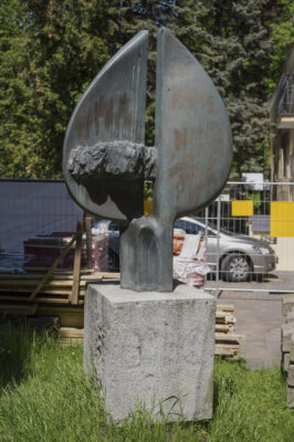 Zdjęcie pionowe wykonane na wprost, na którym znajduje się rzeźba o abstrakcyjnym charakterze wykonana w brązie. Na jej konstrukcje składają się dwa wydłużone półkola, zwrócone ku sobie swoimi średnicami. Na ich dolnych częściach został umieszczony element przypominający zminiaturyzowany tłum ludzi, których ciała zaczynają zlewać się w jedną masę. Cała kompozycja została ustawiona na niskim walcu. Rzeźba znajduje się na kamiennym, jasnoszarym, sześciennym postumencie, na którego jednej ze ścian znajduje się plakietka z napisem: „Kosynierom Gdyni. Zbigniew Zabrocki”.