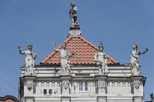 Zdjęcie ukazuje szczyt kamienicy , na której umieszczone są figuralne rzeźby.