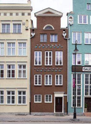 Zdjęcie pionowe ukazuje fasady kamienic - na środkowej można zauważyć dekoracyjny fryz przedstawiający ryby wykonane z ceramiki.