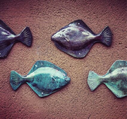 Zdjęcie ukazuje fragment dekoracji z fasady kamienicy, są to ceramiczne flądry w kolorach turkusowym i fioletowym, w dwóch rzędach.