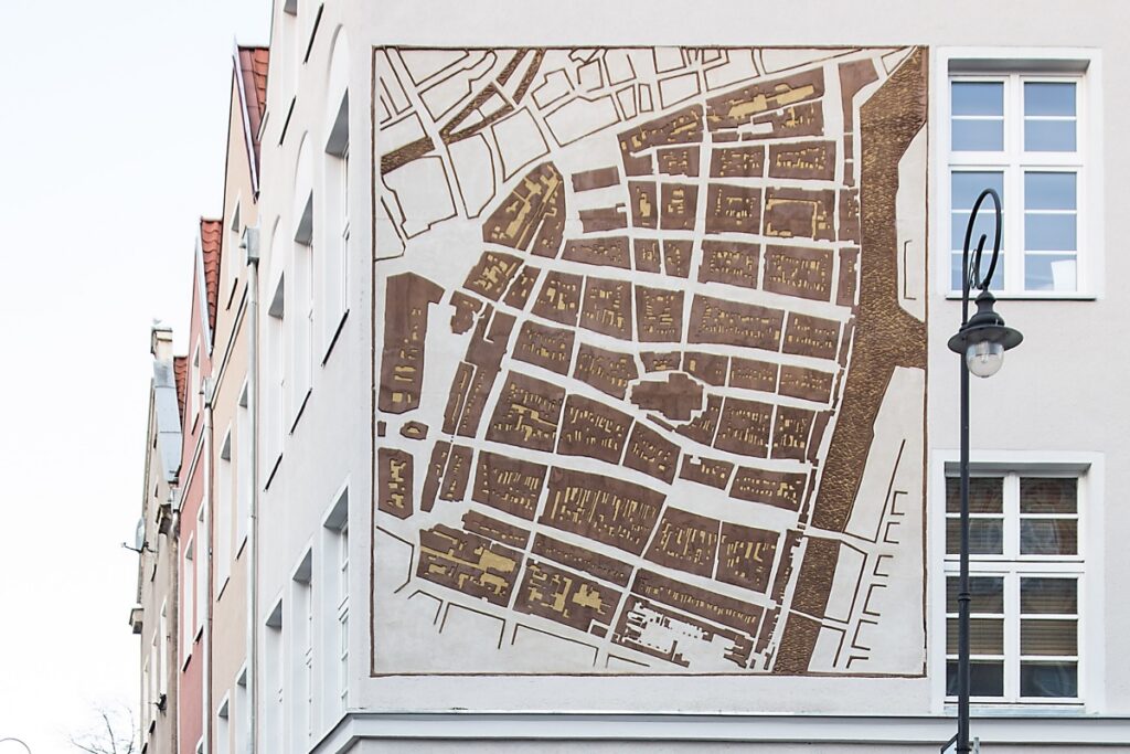 Zdjęcie ukazuje zbliżenie na fasadę, na której wymalowano przedwojenny plan miasta Gdańska, kolorem brązowym na jasnym tynku.