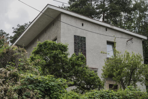 Zdjęcie poziome przedstawiające niski budynek mieszkalny, którego jedna ze ścian bocznych ozdobiona jest prostokątną, ciemnobrązową mozaiką. Jej powierzchnia jej pofalowana i przypomina fale morskie.