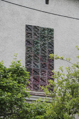 Zdjęcie pionowe ze zbliżeniem na prostokątną mozaikę, na którą składają się kwadratowe płyty w tym samym rozmiarze. Ich powierzchnia jest pofalowana i swoim wyglądem przypomina morskie fale. Kolorystyka mozaiki jest ciemnobrązowa z pojedynczymi, gradientowymi przejściami do bordo i ciemnej zieleni.