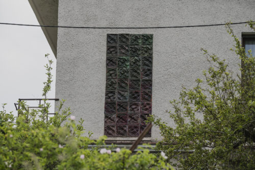 Zdjęcie poziome przedstawiające niski budynek mieszkalny, którego jedna ze ścian bocznych ozdobiona jest prostokątną, ciemnobrązową mozaiką. Jej powierzchnia jej pofalowana i przypomina fale morskie.