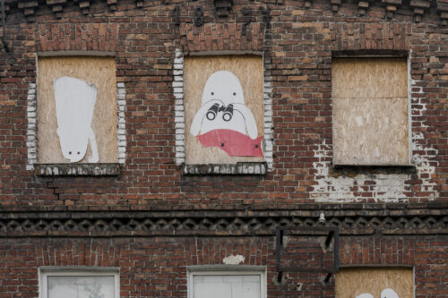 Zdjęcie ukazuje fragment budynku ze zbliżeniem na otwór okienny, w którym umieszczono dyktę z rysunkiem ducha na białym tle.